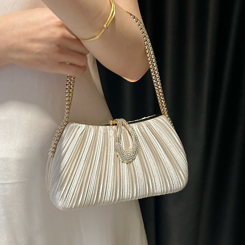 White pleated handbag with gold chain strap held by a person against a neutral background