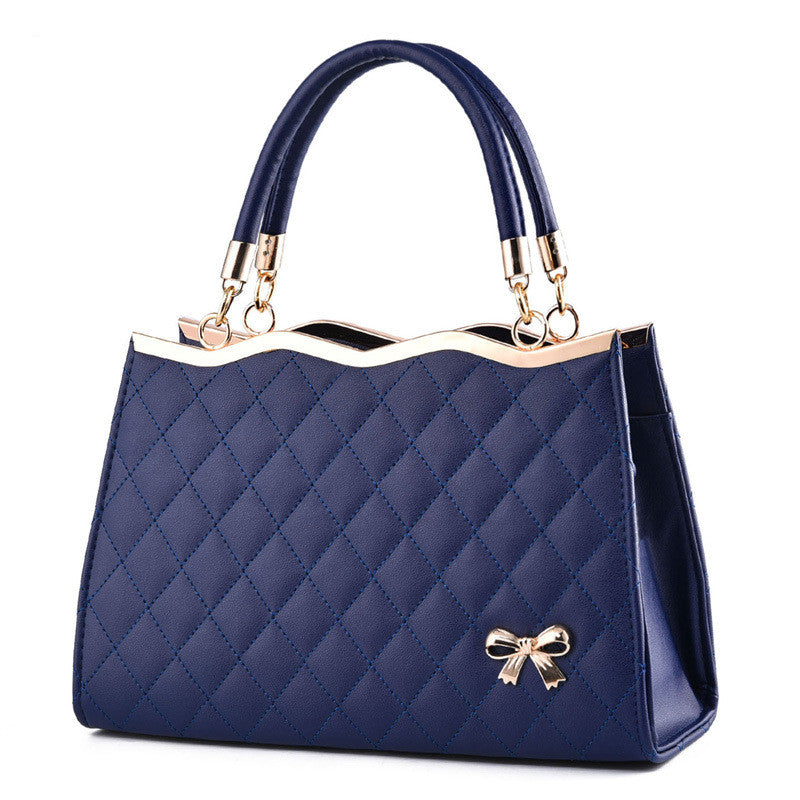 Blue quilted handbag with a gold bow detail on a white background