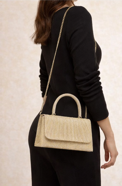 Person wearing a black outfit with a gold handbag on a neutral background