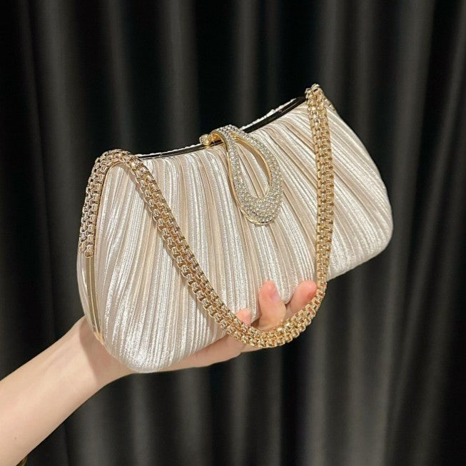 Hand holding a pleated clutch bag with gold chain handle against a black background