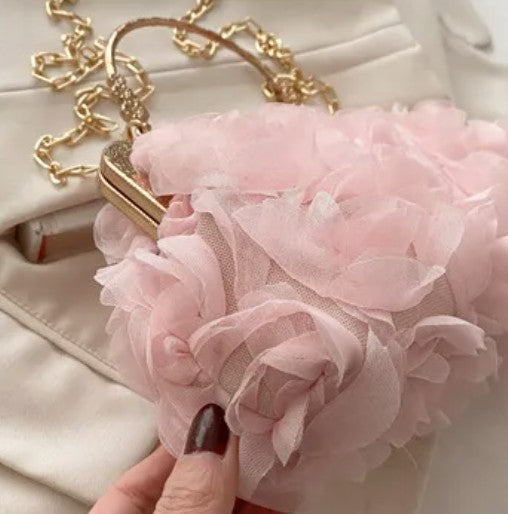 Pink floral clutch held by a hand with dark nail polish, against a light background.