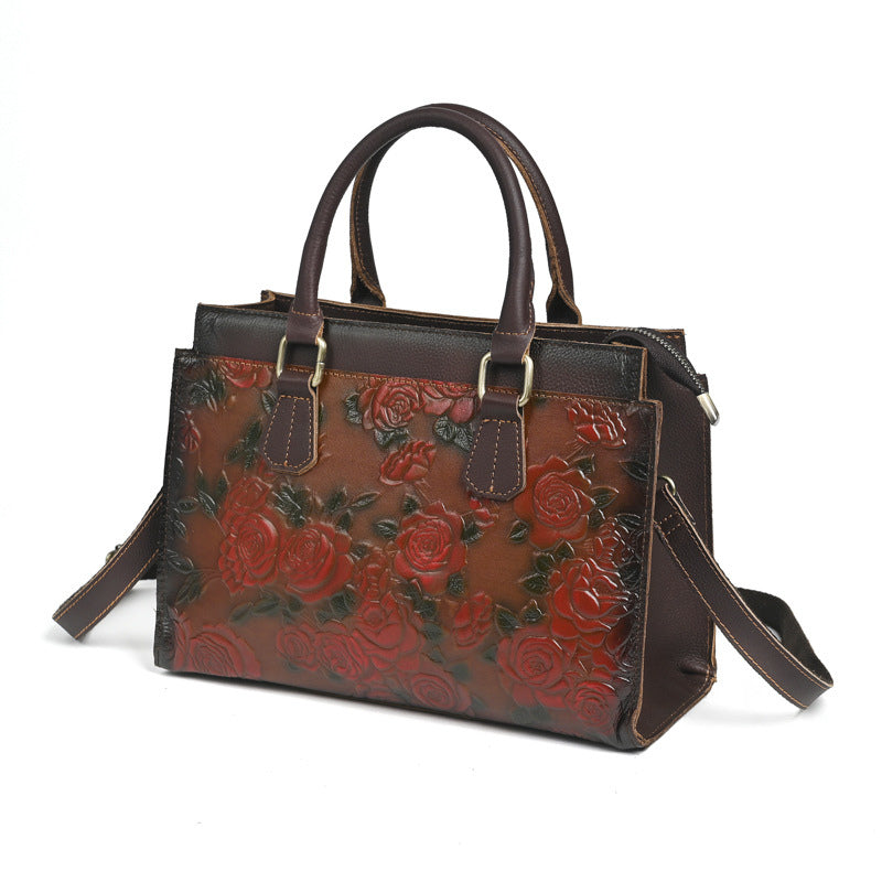 Brown leather handbag with red floral embossing on a white background