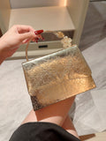 Gold clutch bag with textured surface held by a hand against a neutral background