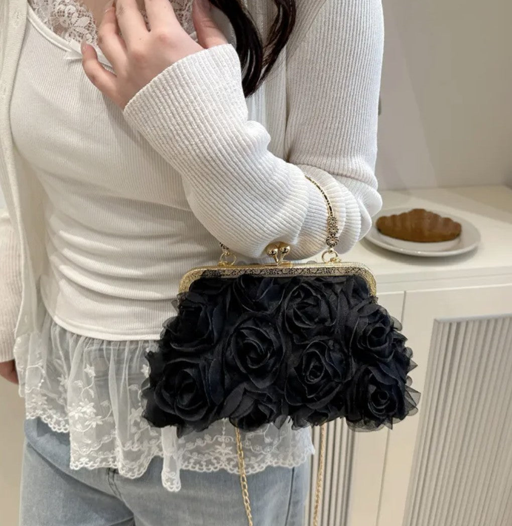 Person holding a black rose handbag with a white lace top.