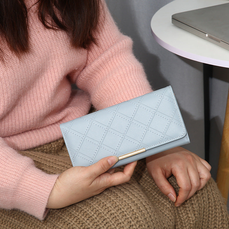 Person holding a light blue quilted wallet with a pink sweater and brown pants.