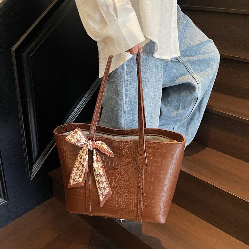 Brown leather handbag with a decorative bow held by a person on wooden stairs.