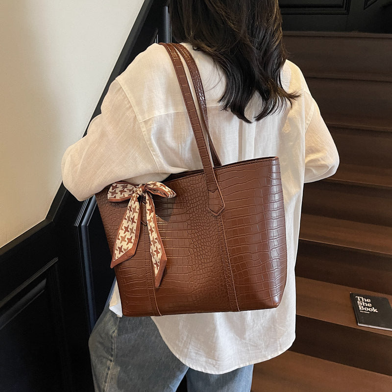 Person holding a brown handbag with a decorative ribbon walking up a staircase