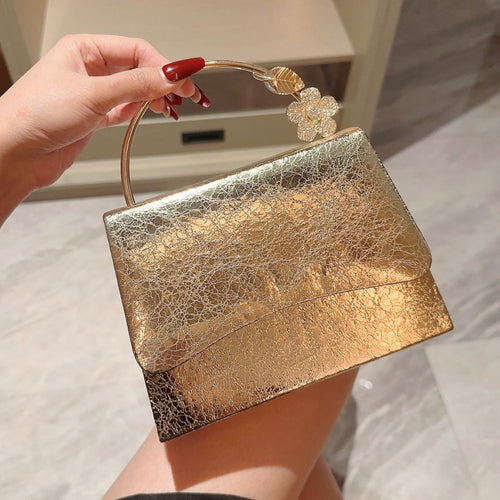 Gold clutch bag with floral handle held by a hand against a marble background