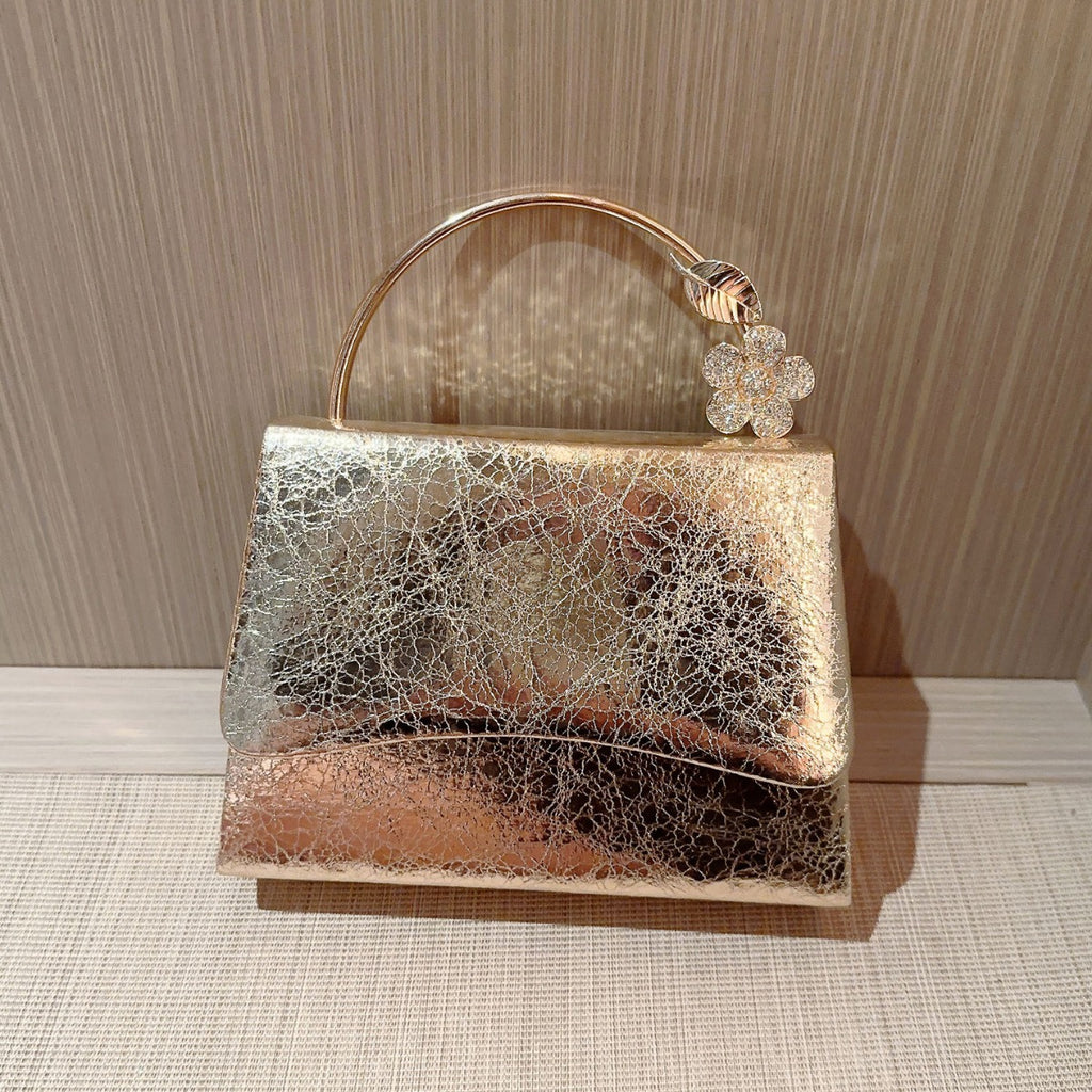 Gold and silver handbag with a decorative flower on a textured surface