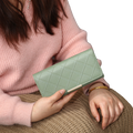 woman holding a green quilted wallet against a neutral background
