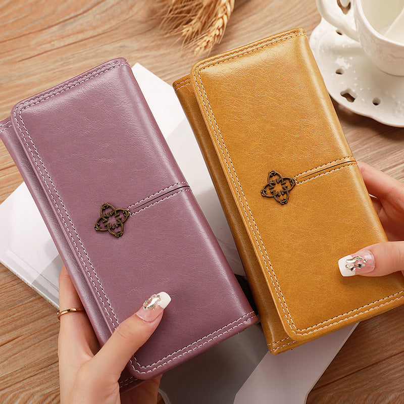 Two leather wallets, one purple and one orange, held by hands on a wooden surface.