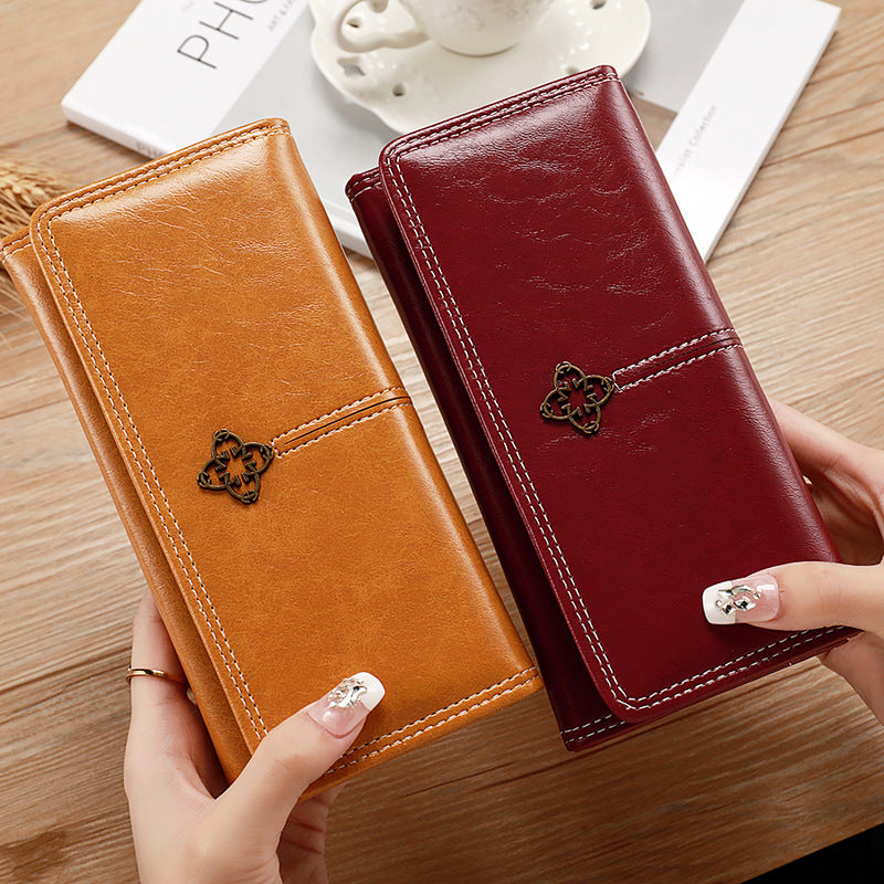 Two leather wallets, one orange and one red, held by a hand on a wooden surface.