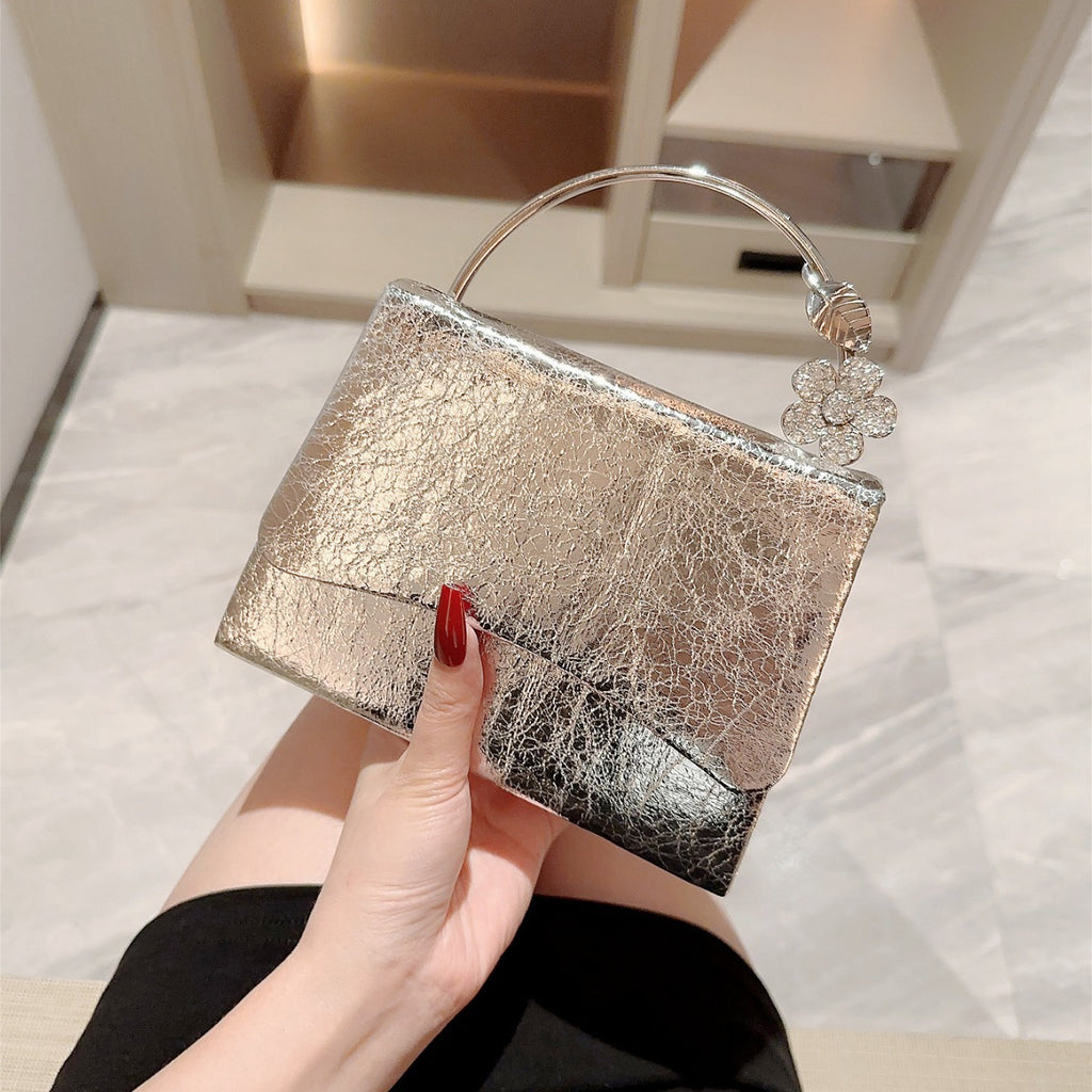 Silver textured handbag with floral charm held by a hand against a neutral background