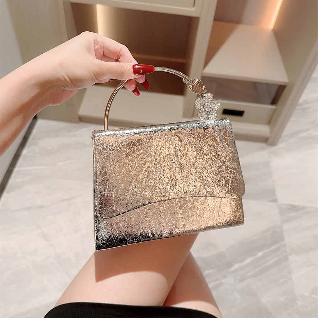 Hand holding a glittery handbag with a decorative flower on a neutral background