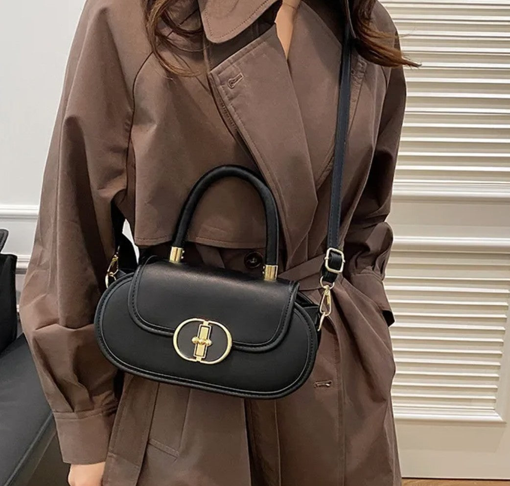 Person wearing a brown coat holding a black handbag with gold accents.