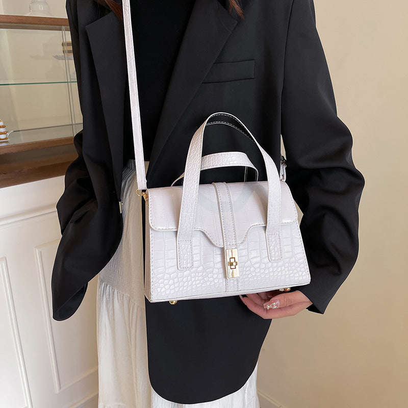 Person wearing a white handbag with a gold clasp in an indoor setting as a crossbody
